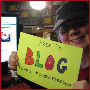 Laurel holds a "Free to Blog" sign with the hashtags #WPFD and #PressFreedom